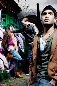 Three teenagers in an alley with graffiti and a mill chimney in the background