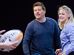 Rhys in rehearsals with Bethan Witcomb looking towards someone throwing a rugby ball towards them