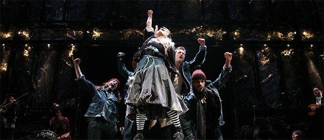 a group of people in theatrical lighting punching the air excitedly