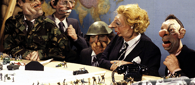 a caricature puppet of Margaret Thatcher at a war meeting with colleagues, at a table with miniature military figures and vehicles, from the Spitting Image tv show
