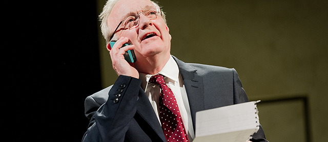 A middle aged man in suit and tie using a mobile phone and holding a piece of paper 