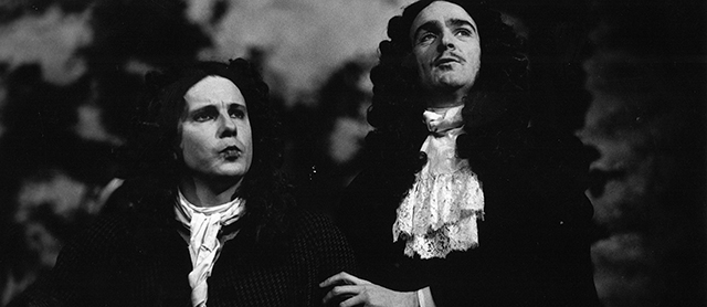 Black and white photo of two men in restoration wigs and clothes.