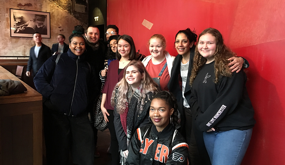 a group of young people smiling, standing against a red wall