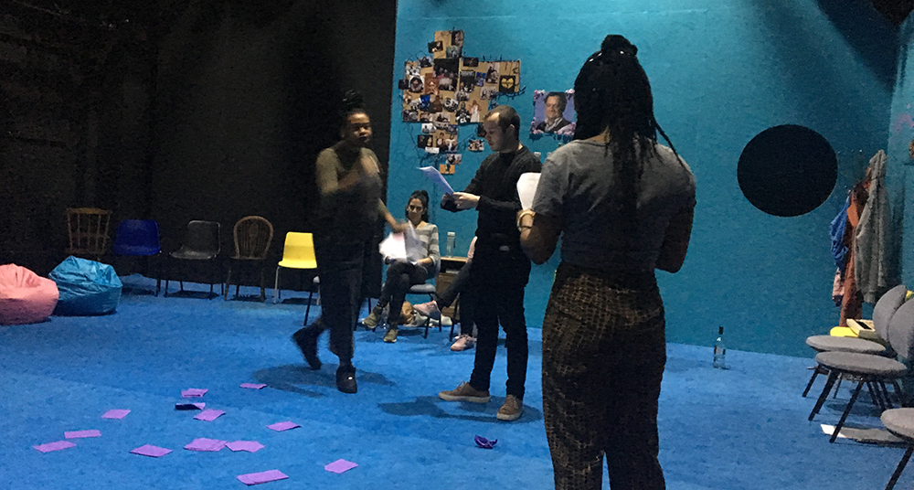 Young actors rehearse with scripts on a blue-coloured theatre set.